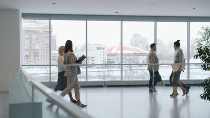 Businesspeople men and women are walking in office hallway talking discussing business in lobby. Workspace and corporate lifestyle concept.