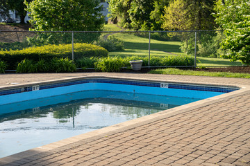 Swimming pool with concrete pavers just after opening for the season with green water and debris