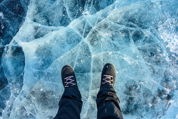 A foot of tourist standing on the cracks surface of frozen lake Baikal in the winter season of...