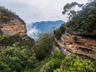 Giant strata of  red rock frame vista of canyon and mountains in the distance in Blue Mountain National Park, New South Wales, Australia. 