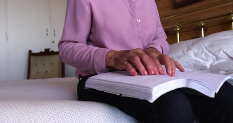 Woman reading a braille book in bedroom at home
