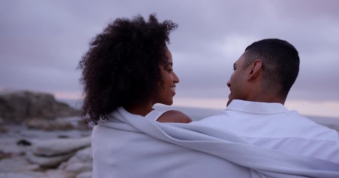 African American couple wrapped in blanket on beach