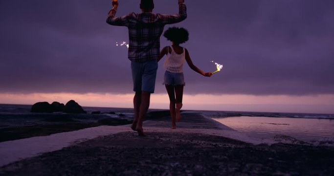 African American couple running with sparklers on concrete pier at beach