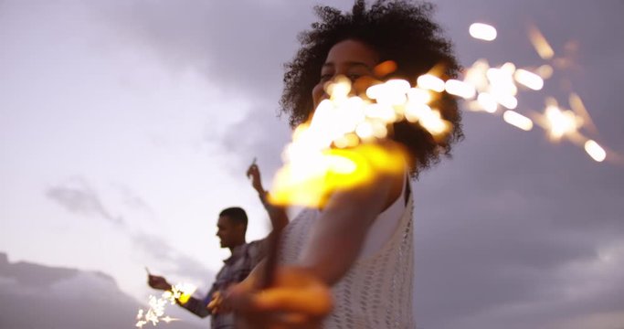 African American couple dancing with sparklers on beach at dusk