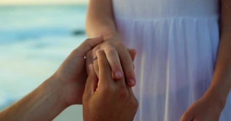 Man putting ring on woman finger at beach