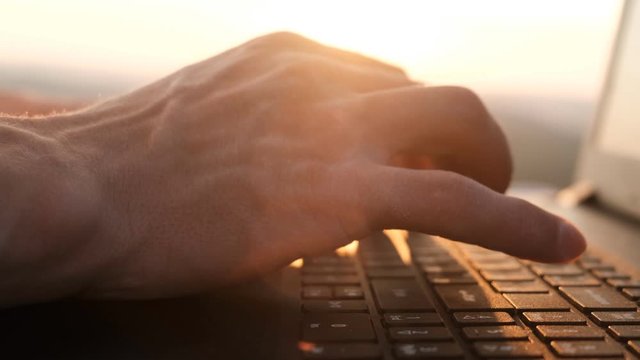 Close-up of hands typing on the keyboard at sunset.Working on a laptop outdoors, slow motion.