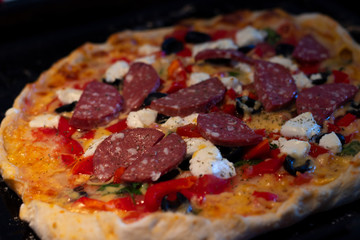 hot tasty delicious rustic homemade american pizza with tomato gherkin salami olives with thick crust on black table