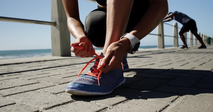 Fit woman tying shoelaces on a promenade at beach