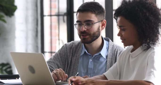 Young smart manager in eyeglasses showing corporate computer software apps to african american female colleague, head shot. Focused two multiracial teammates working together on project in office.