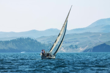 Yacht regatta with an color sail against the green slopes of the mountains on the sea. Wide panorama