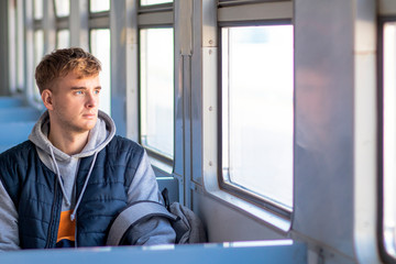 A young one man is sitting on the train, a sad guy is looking out the window on the train.