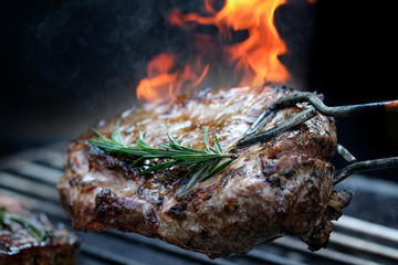 Grilled steak meat on the grill of the grill that has a flame