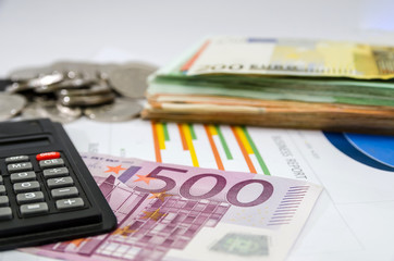 Euro banknotes with calculator and coins on the background of business charts. Business concept.