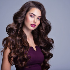 Face of a beautiful woman with long brown curly hair. Fashion model with wavy hairstyle. Attractive young  girl with curly hair posing at studio. Female face with purple makeup. Violet make-up.