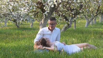 Naklejka na ściany i meble young guy and girl in blooming apple trees in the garden