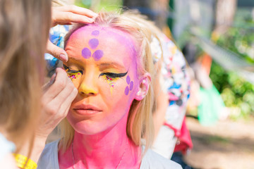 A woman's face painted in a fairy-tale character. Applying a pink aqua-color to the face.