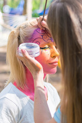 A woman's face painted in a fairy-tale character. Applying a pink aqua-color to the face.