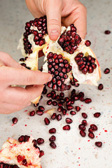Male hands peel pomegranate on a white texture table background. Pomegranate seeds are scattered....