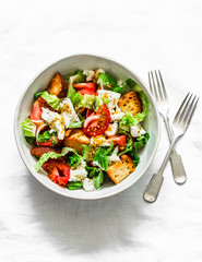 Simple salad with fresh tomatoes, crispy ciabatta, mozzarella cheese, green salad with olive oil, mustard, lemon dressing on a light background, top view