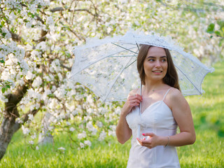 girl with a white umbrella in blooming apple trees in the garden