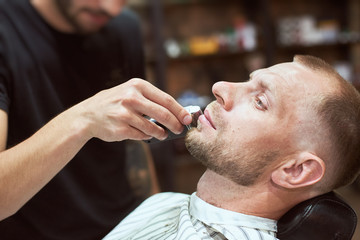 Unrecognizable blurred hairdresser is doing a perfect beard shape to his male client at barber shop, time to take care of oneself, relaxation