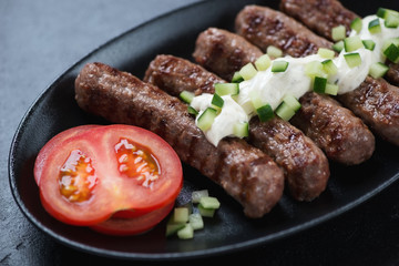 Close-up of bbq serbian cevapi or cevapcici sausages topped with kajmak cheese, selective focus