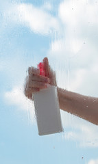 washing the window with a cleaner; behind a wet window, a clear sky and a hand with a bottle