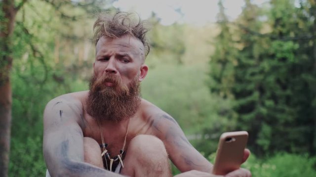 Charismatic, Bearded Aboriginal with Mustache Takes Selfie on Smartphone. Prehistoric Primeval Male Makes Grimaces and Laugh. Technology Progress, Evolution. Closeup.