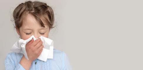 Cute blond Caucasian girl blows her nose in a paper handkerchief. Banner. Illness, flu, sick...