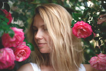 blond woman smiling in a flowering bush of pink roses