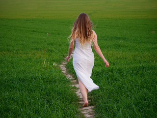 Obraz na płótnie Canvas girl in a long white dress on a green field