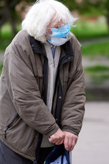 An old grandfather in two medical masks, with a stick in his hands, with overgrown hair and eyebrows asking for money. A beggar outside the store entrance. poor person. quarantine. covid-19