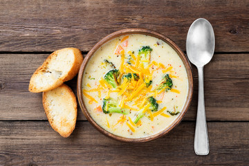 Wooden bowl of creamy broccoli cheddar cheese soup with toasted bread top view	
