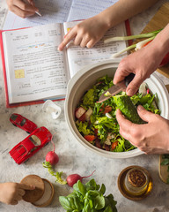 A multi-tasking mother prepares salad and checks her daughter’s lessons and plays with the baby at the same time during the isolation period.