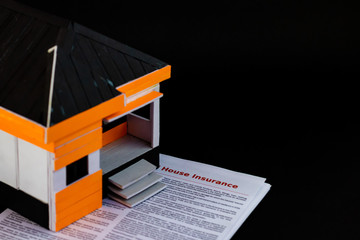 High angle shot of a home model with house insurance papers below, on black background.