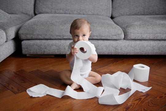 Funny baby chewing on toilet paper roll in living room