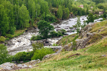 Fototapeta na wymiar Beautiful landscape with big stones in water riffle of mountain river. Powerful water stream among boulders in mountain creek with rapids. Fast flow among rocks in highland brook. Small river close-up