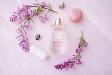 
glass perfume bottle with delicate lilac flowers and seashells on a pink background