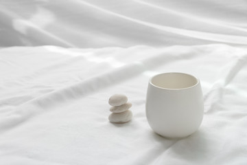 clean white ceramic tea drinking cup and pebble rock in wellness zen Japanese style on fabric soft background
