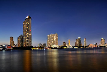 Fototapeta na wymiar Golden blue sky at Chao Phraya River with lighting on the building in cityscape.