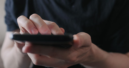 Closeup young man in black t-shirt use smartphone while sitting on a couch