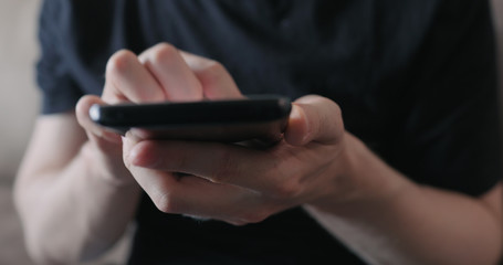 Closeup young man in black t-shirt use smartphone while sitting on a couch