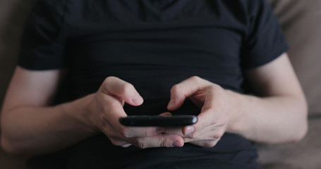 Closeup young man in black t-shirt typing messages on smartphone working from home