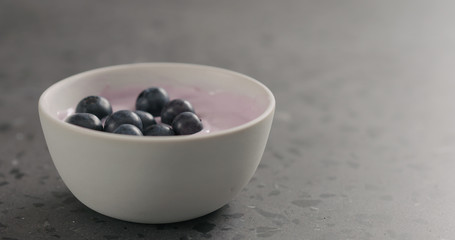 ripe blueberries fall in blueberry yogurt in white bowl with copy space