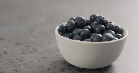 ripe blueberries in white bowl on concrete background with copy space