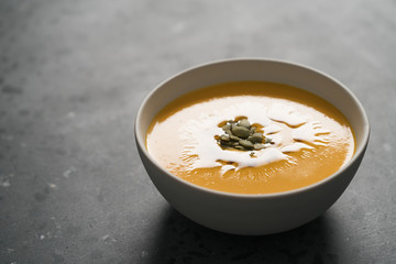 Pumpkin soup decorated with pumpkin seeds oil in white bowl on concrete background with copy space