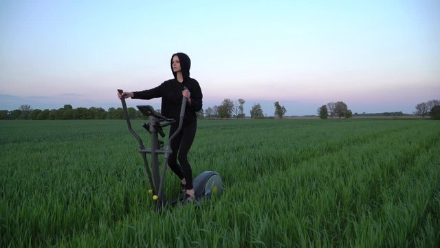 Dolly shot. Green fitness. A young woman is working out on stepper in a green field.