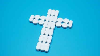 The white pill is arranged as a symbol of the cross on blue background, Medicine concept, blank space for design..