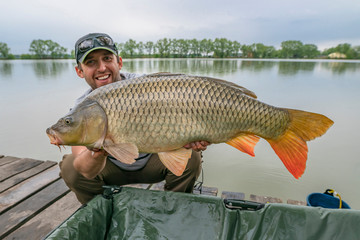 Carp fishing. Fisherman with fish trophy in hands at lake