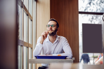 Young smiling man elegantly dressed sitting in fast food restaurant, eating french fries and taking a break from work.